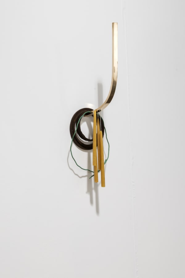 installation view of a wall mounted sculptural object consisting of bronze, salvaged iron, copper wire covered in plastic, beeswax candles