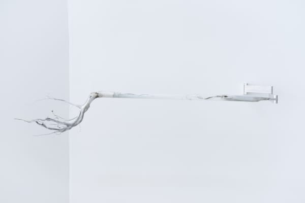 An image of a silver root connected to a white wall by electric cables, acrylic tube, and aluminum rod.