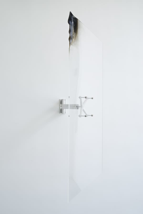 A burned acrylic sheet attached to a white wall by an aluminum spider bracket.