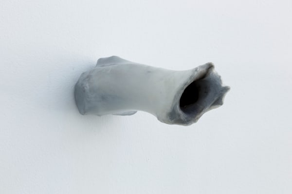 An image of a cylindrical shaped cow bone shard hanging on a white wall.