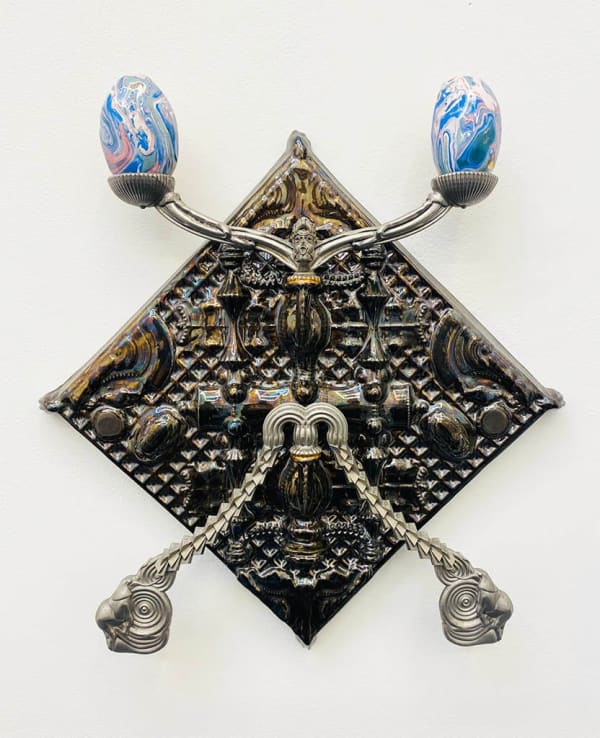 silver candelabra hung on a white wall holding two multicolored eggs