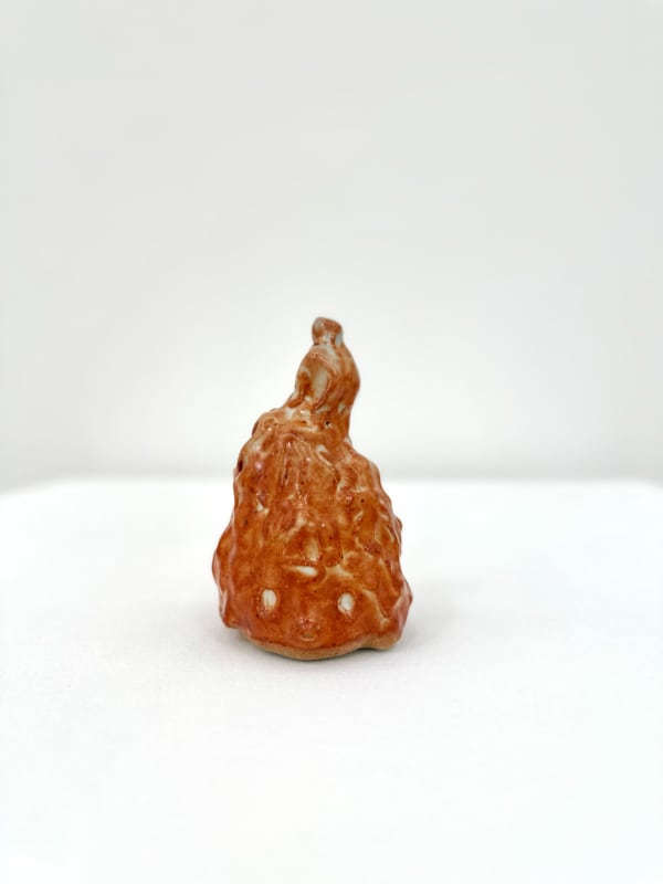 Ceramic sculpture of a head with a pointy top in a burnt orange glaze.