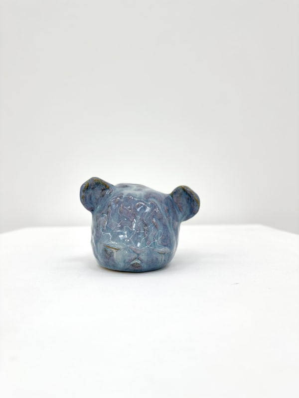 Ceramic sculpture of a bears head with its eyes closed in a blue purple glaze