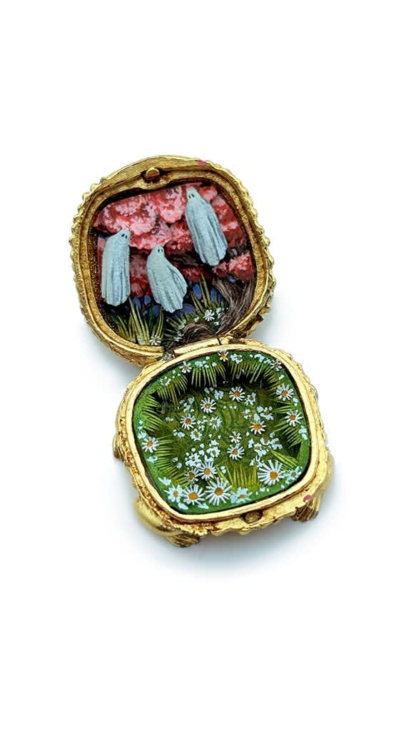 hand-cut watercolor collage in antique cosmetic compact by Shannon Taylor with three hovering ghost on red sky background and white daisies below