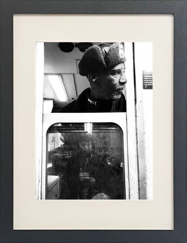black and white photo of subway train conductor looking out the window in black frame