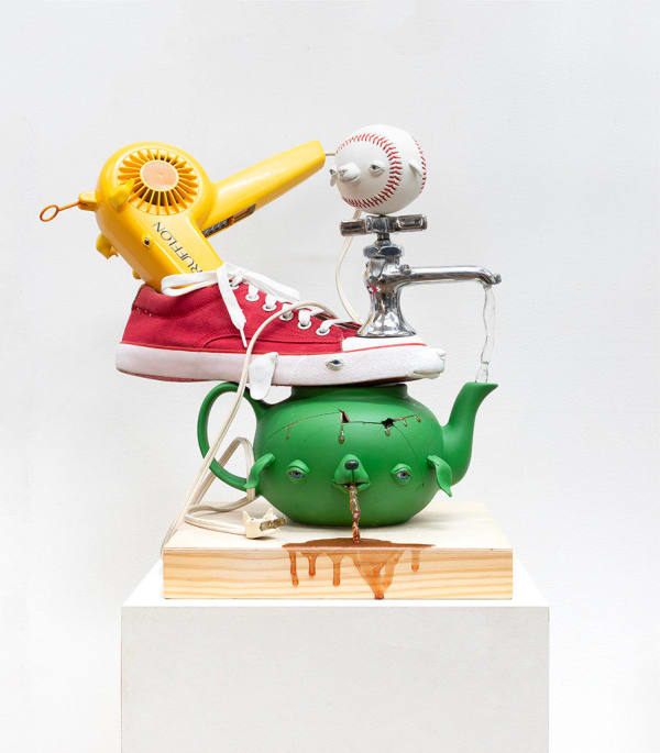 green teapot with a dog face spitting up tea and shoes, a hair dyer, a faucet spout and a baseball stacked on top