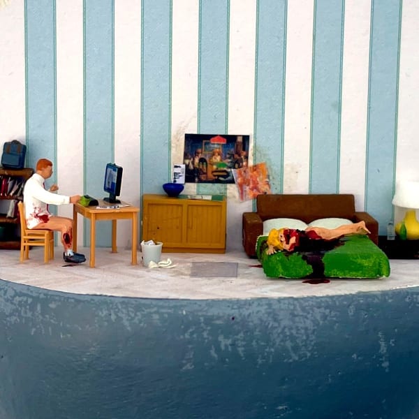 bloodied man sitting at desk with computer while a bleeding woman lays on a bed