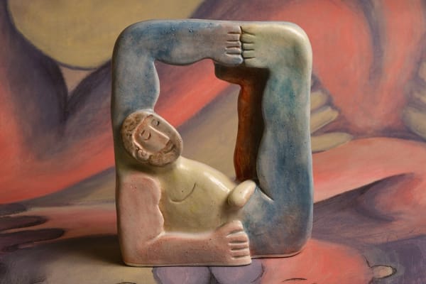 Statue of a nude man reclining with his leg and arm up with a red, blue, and yellow glaze