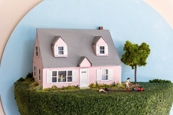 miniature diorama by Abigail Goldman of a woman running over a body with a lawnmower in the front yard of a pink house