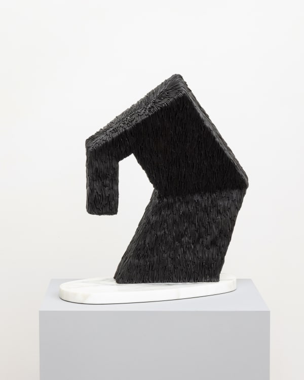 Free-standing bronze sculpture of a tall angular shape that is bending over and perched on a rounded marble base. The sculpture is cast with a surface texture resembling shaggy hair and treated with a black patina.