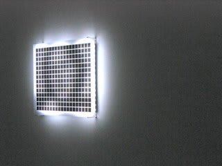Still image of a rectangular piece with multiple white LEDs behind a thick block of acrylic which has a grid of black squares on its surface The LEDs display blurred scenes taken from old family home movies
