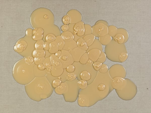 Circular droplets of tan rubbery substance against linen background. Droplets cluster to make one larger blob shape. Some of the droplets layer on top of each other to jut outward in three-dimensional protrusions.