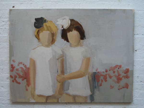 Two girls dressed in white, one with blonde hair and black hairpiece and the other with brown hair and white hairpiece, pose in front of red flowers. The girl on the right holds onto the arm of the girl on the left.