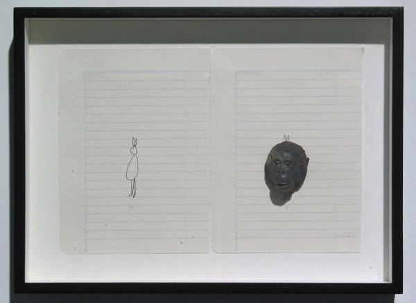 Two pieces of loose leaf paper are placed next to each other and framed. On the paper to the left a small bunny-like cartoon figure is loosely drawn. To the right a larger three dimensional sculpted monkey head is mounted off center