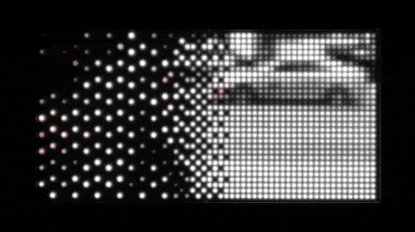 Gif of rectangular piece with multiple LEDs behind Plexiglass that displays a highly pixelated and blurred city street scene The people to the right side of the image are black and white and have more clarity while the figures at the left side are colorful but very blurred and abstracted