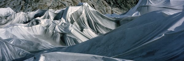 Digital panoramic landscape photograph of dirty white tarps blanketing the rough multiple ridged surface of the Swiss Rhône Glacier during the day