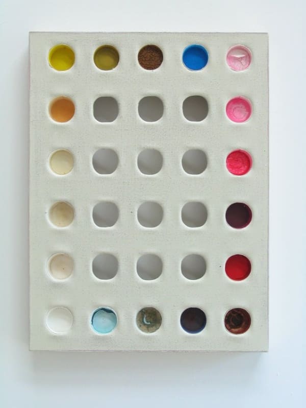 Six by six grid of multi-colored circular found objects that are inserted into a pale beige painted rectangular canvas so that parts of the surface recess into depth