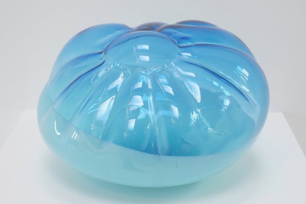A cushion-like blown-glass sculpture, top two-thirds translucent blue, bottom one-third opaque blue.