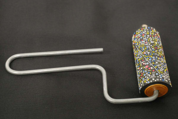 Top angled view of a metal-handled paint roller on a black background. Variety of white, blue, red, and yellow 1D cutouts attached to black roller head.