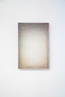 Layers of multi-colored threads strung across a rectangular wooden and plaster panel create the effect of a large white glowing center that is enclosed by a light gray border at the top which fades into a beige border at the bottom