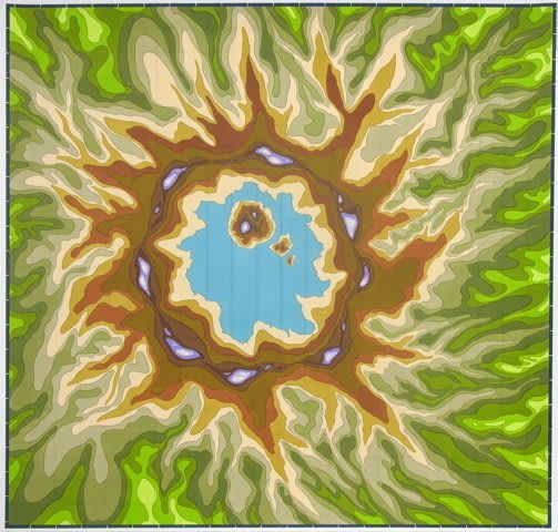 Multiple yellow green brown and blue ambiguous sun like shapes come together to allude to a topographic map of a water filled volcano