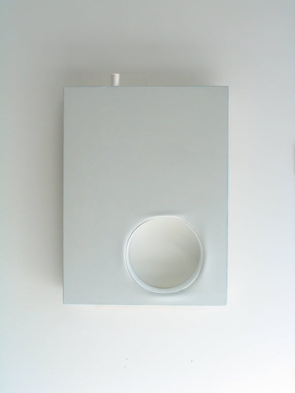 A circular object is inserted into a pale blue painted rectangular canvas A small white spool of thread rests vertically on the top edge of the canvas