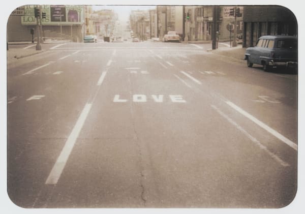 Enlarged print of an original photograph of a performance piece The photo captures the urban nineteen fifties landscape scene of the word LOVE painted in white onto San Francisco’s Oak Street
