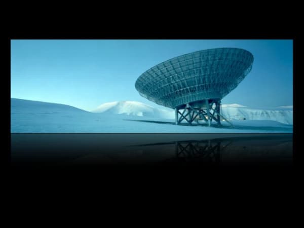 Blue toned digital panoramic landscape photograph of a giant scientific instrument in the middle of an arctic tundra whose shape resembles a large satellite dish