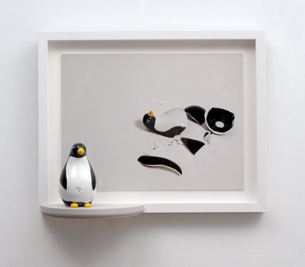 Framed cibachrome print of a digital photograph which depicts a shattered black and white penguin figurine. At the lower left side of the framed photo a white painted wooden shelf provides a platform for the same penguin figurine however this figurine is whole and unbroken