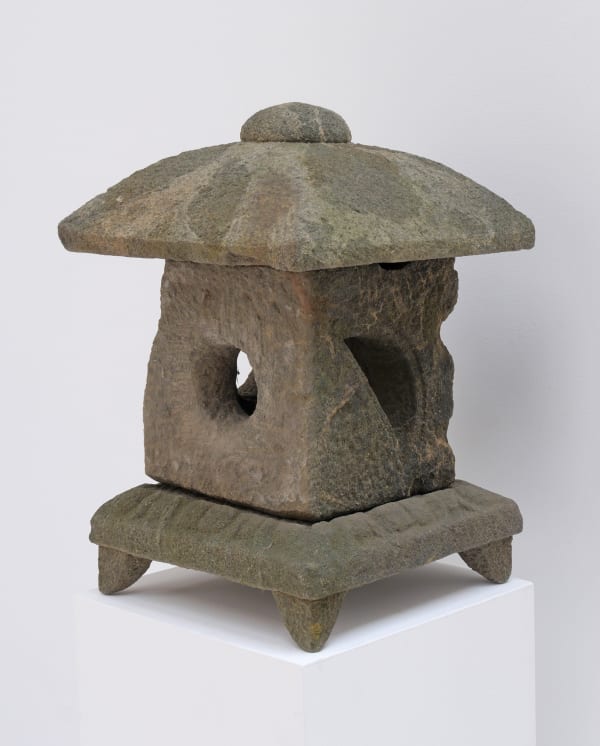 Weathered stone lantern with square base and feet, square body with hole in the center, and domed topper.