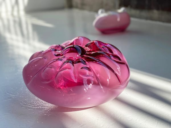 Two pink, blown-glass sculptures arranged on a white floor.