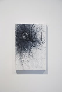 White painted background with multiple hasty black ink brush strokes which appear to sprawl out of a smaller and a larger negative space circle towards the top portion of the canvas