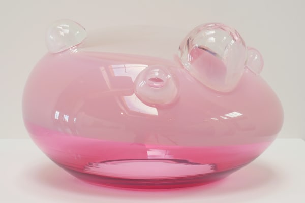 UFO-shaped glass sculpture. Top 2/3 opaque blush-pink, bottom 1/3 pink. Clear top with clear bubbles of varying sizes.