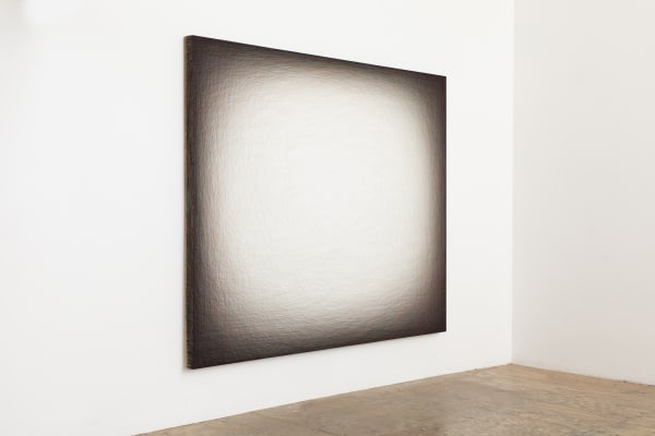 Layers of multi-colored threads strung across a rectangular wooden panel to create the effect of a glowing white center surrounded by a dark border