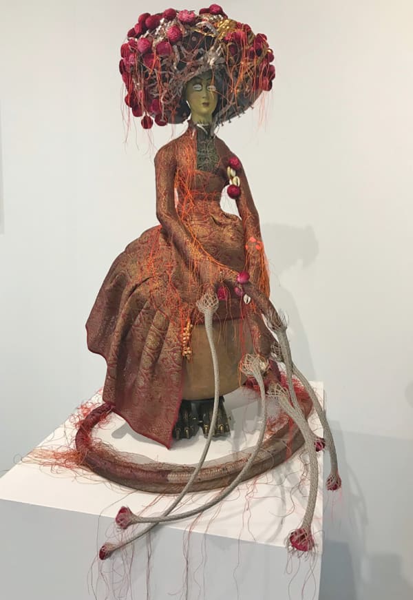 An image of a victorian doll in a vintage silk wedding sari with gold thread brocade, vintage brass claw furniture cap, steel, copper leaf, copper nails, wood, silk, cotton, sequins, gourd, polyester threads, wax, cowry shells, eyelashes, silk trim, pheasant feathers on felt hat plates.