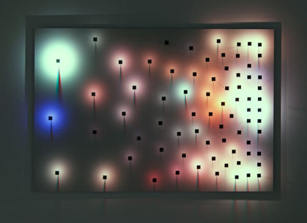 Still image of a rectangular aluminum board with metal rods arranged more densely towards the right side. On the ends of each rod multi-colored LEDs are mounted and they shine soft glowing circles on the surface of the board