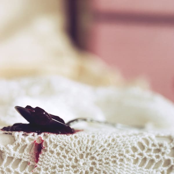 Chromogenic print of a zoomed in digital photograph of a spoon full of red purple jam on top of a white bed The spoon full of jam is staining the white crocheted bed cover it was left on and leaving behind several fruit clumps