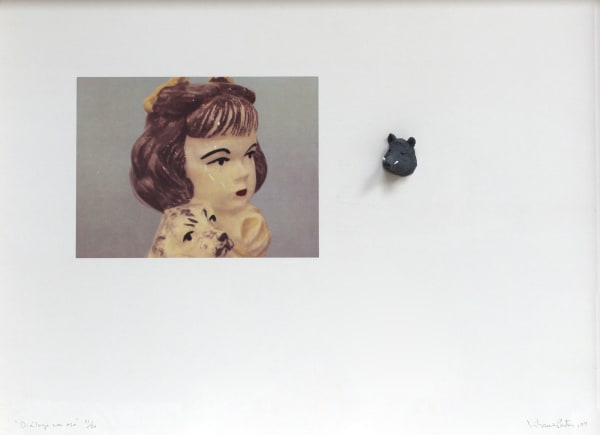 Lithograph of a zoomed in photo of the head of a white porcelain girl. A tiny boar head that was molded and painted black is mounted to the right of the girl. The porcelain girl and board head appear to be side eyeing each other