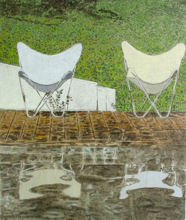Two white lawn chairs stand on tiled patio in front of grassy background. Chairs are reflected in pool in the foreground.