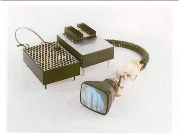 Electronic sculpture made out of custom made electronics that take the shape of two small boxes. From one of the boxes a black coiled tube covering several wires snakes out of the end and reveals the small LCD screen at its end. The LCD screen displays a blue tinted hand