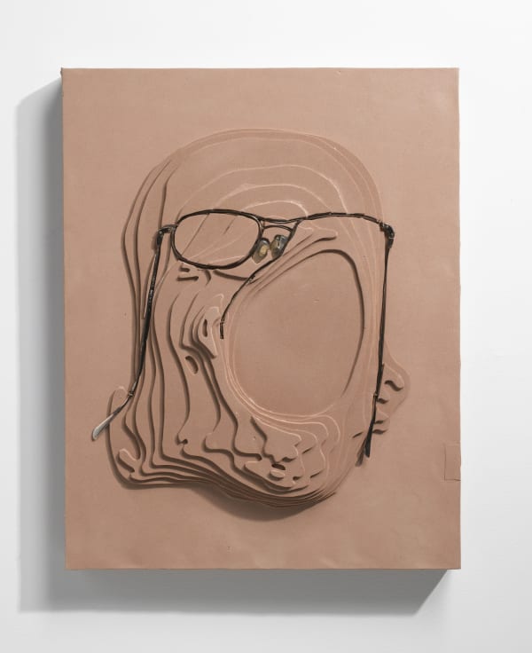 Multiple carvings into beige foam create topographical layers. Warped eyeglass frames are sunken into the top of the foam layers and form an abstract portrait of the artist’s face
