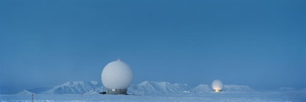 Blue toned digital panoramic landscape photograph of two dome shaped scientific hubs amongst the icy tundra