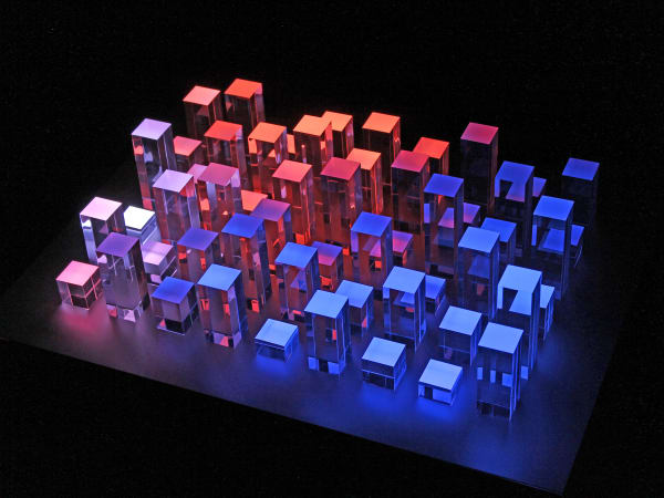 Still image of multiple colorful LEDs shining up through acrylic blocks of varying heights on the surface of a pedestal