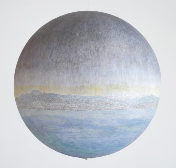 A hanging sphere covered in a drawing of a light blue body of water, a blue and white mountainous landscape, a yellow band and a purple-grey starry sky