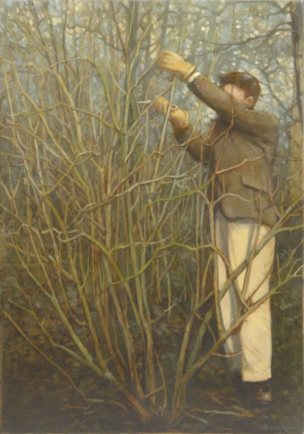 A man in a suit standing in a forest is cutting a branch off of a small leafless shrub.