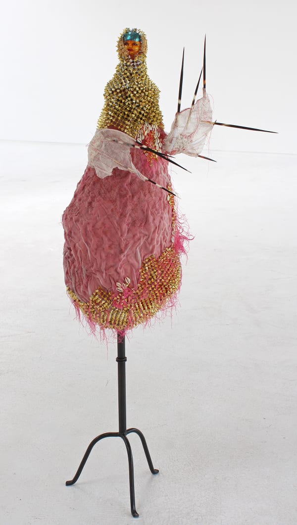 An image of a vintage porcelain doll head with cotton thread, paper mache vessel base, silk fabric with printing, porcupine needles, silver blue leaf, plastic trim on a steel stand.