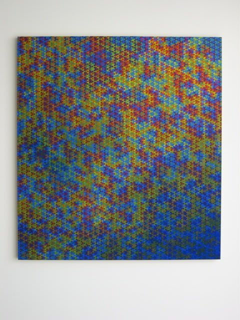 Multi-colored asterisk shaped forms morphing and moving in waves against each other which then fade into a dark blue towards the bottom right corner of the piece