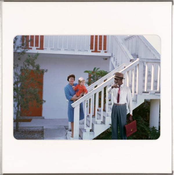 A white woman holding a toddler on the bottom of a staircase with artist, Omar Diop standing in front of the railing looking at her. By Lee Shulman & The Anonymous Project.