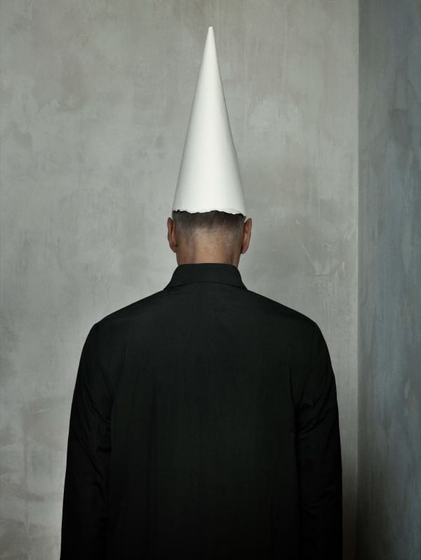 Erwin Olaf self portrait from behind, artist wearing dunce cap and looking at wall, by Erwin Olaf
