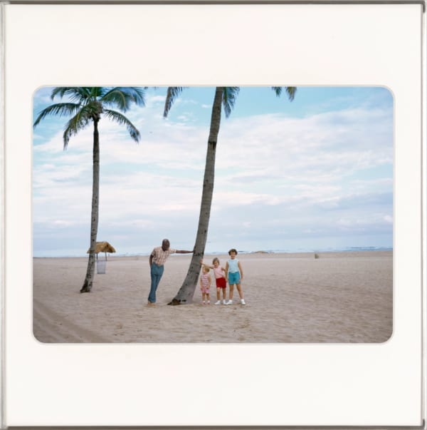 Artist Omar Diop leaning against a palm tree on the beach smiling down at three white children posed next to the same palm tree. By Lee Shulman & The Anonymous Project.